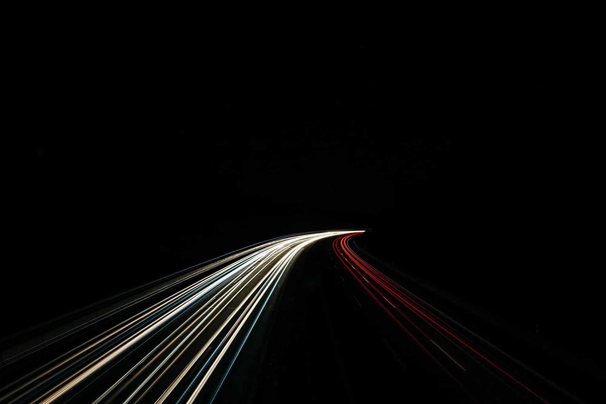 Long-exposure photograph of red and white light trails along a dark highway at night